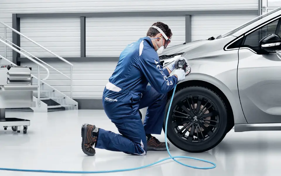 Profissional realizando reparo na lateral de um carro prata na oficina