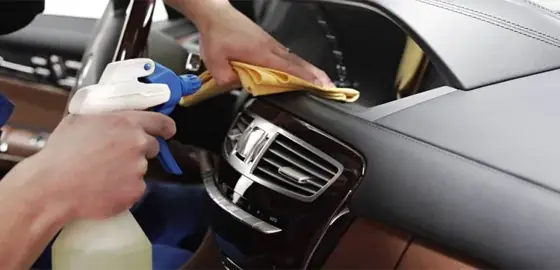 Profissional limpando o painel e as saídas de ar de um carro com pano e borrifador
