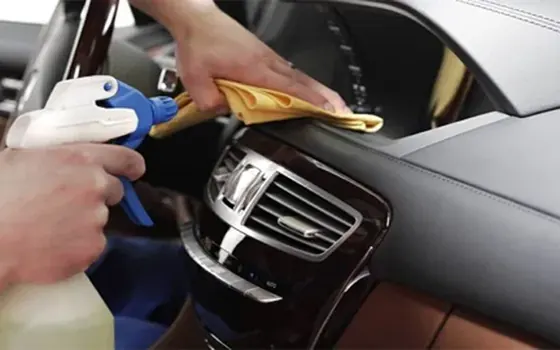 Profissional limpando o painel de um carro com pano de microfibra e borrifador