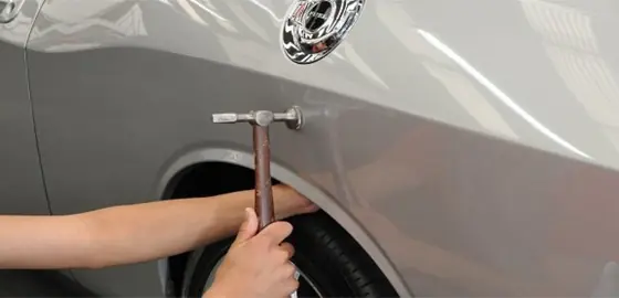 Profissional usando martelo de funileiro na lateral de um carro prata