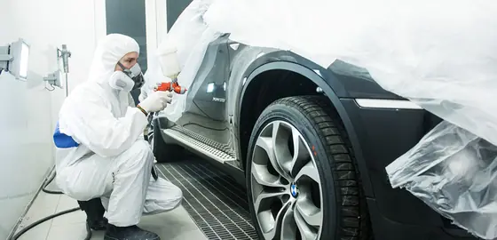 Pintor automotivo aplicando tinta na lateral de um veículo